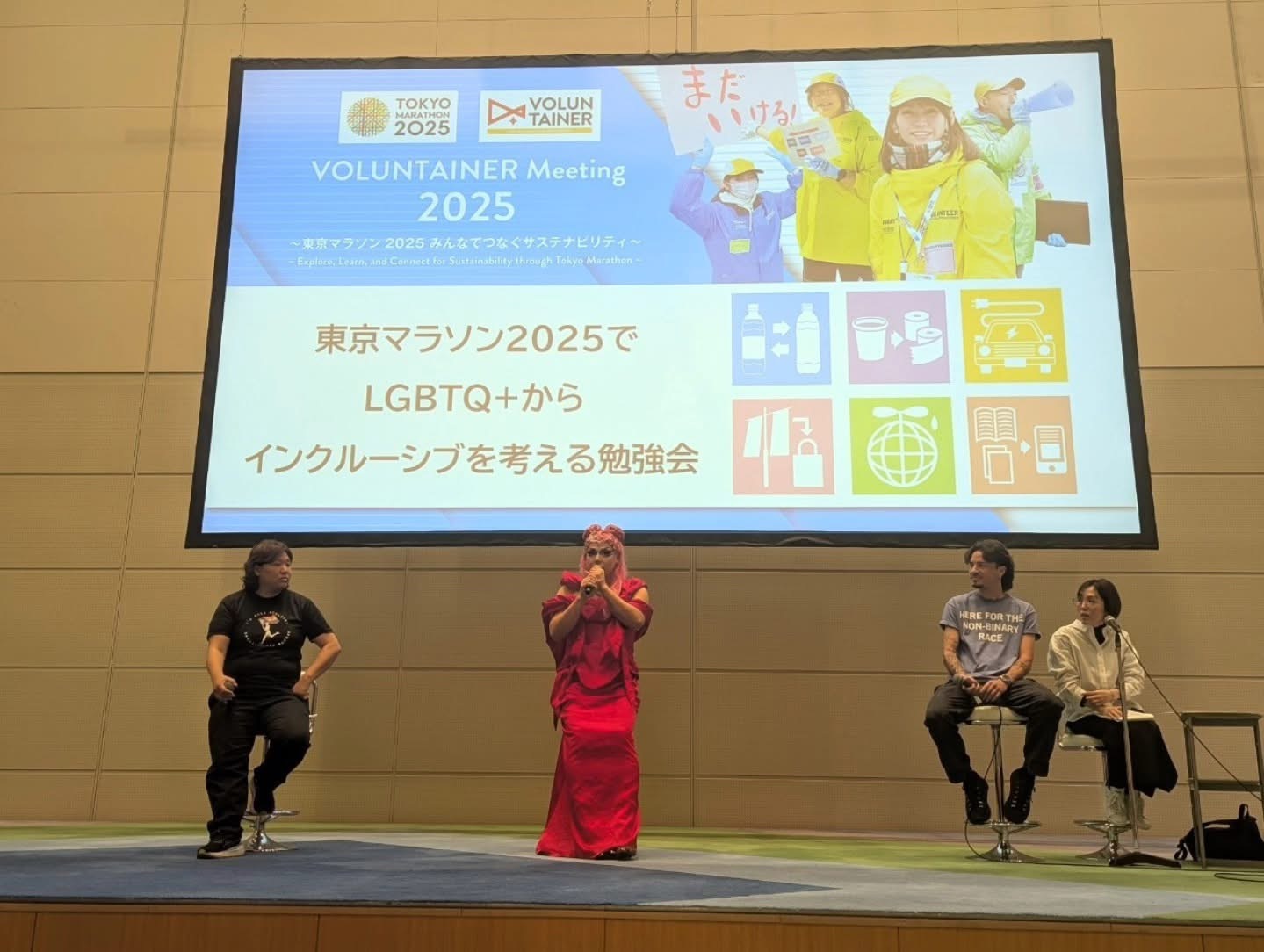 東京マラソン2025でLGBTQ+からインクルーシブを考える勉強会というトークイベントの写真。 後ろに大きなモニターがあり、ステージには左からプライドハウス東京スポーツチームの野口亜弥、ドラァグクィーンのラビアナ・ジョローさん、ノンバイナリーのランナーであるカル・カラミアさん、日英通訳のスタッフの方が座っている。
